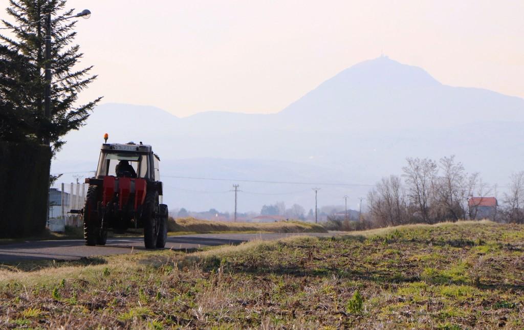 Vue de la Limagne avec champs, tracteur et la silhouette du Puy-de-Dôme au loin